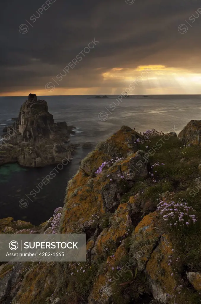 England, Cornwall, Land's End. Rays of sunlight breaking through storm clouds over Longships Lighthouse, viewed from Land's End at sunset.