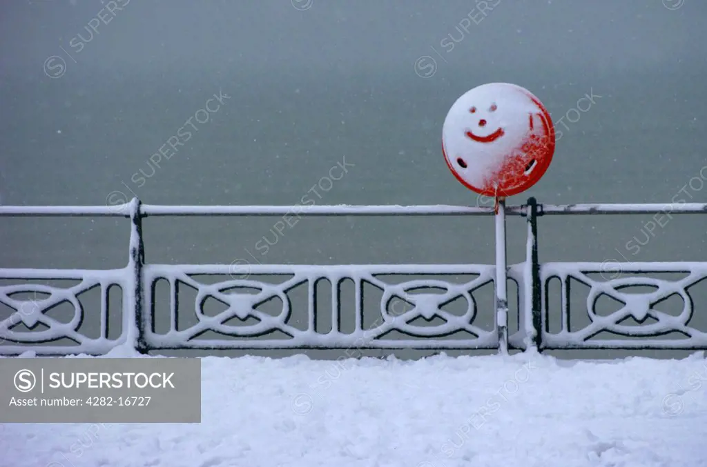 England, City of Brighton and Hove, Brighton. A smiley face drawn in the snow covering a red sign on the seafront at Brighton.