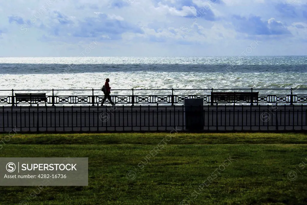 England, City of Brighton and Hove, Hove. A lone figure walking along Hove promenade with the sea in the background.