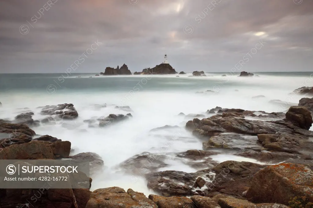 Channel Islands, Jersey, St Brelade. Rough seas around La Corbiere Lighthouse at sunset. The lighthouse was the first in the British Isles to be built from concrete.