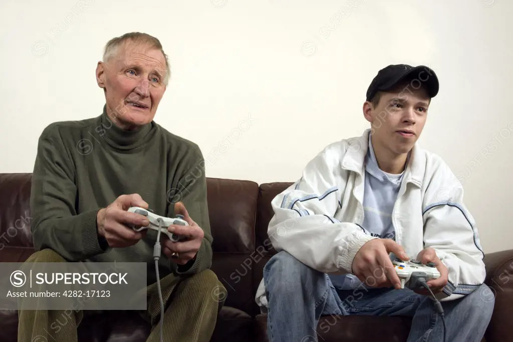 England, County Durham, Durham. A grandfather and his grandson sitting on a sofa playing a computer game.