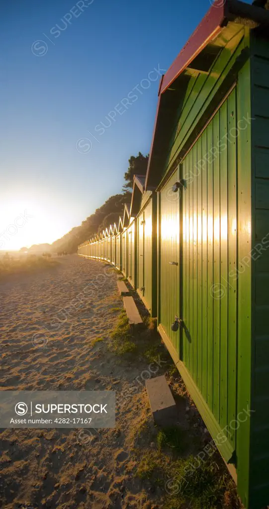 England, Dorset, Christchurch. Sunrise over beach huts stretched out along Avon Beach in Christchurch.