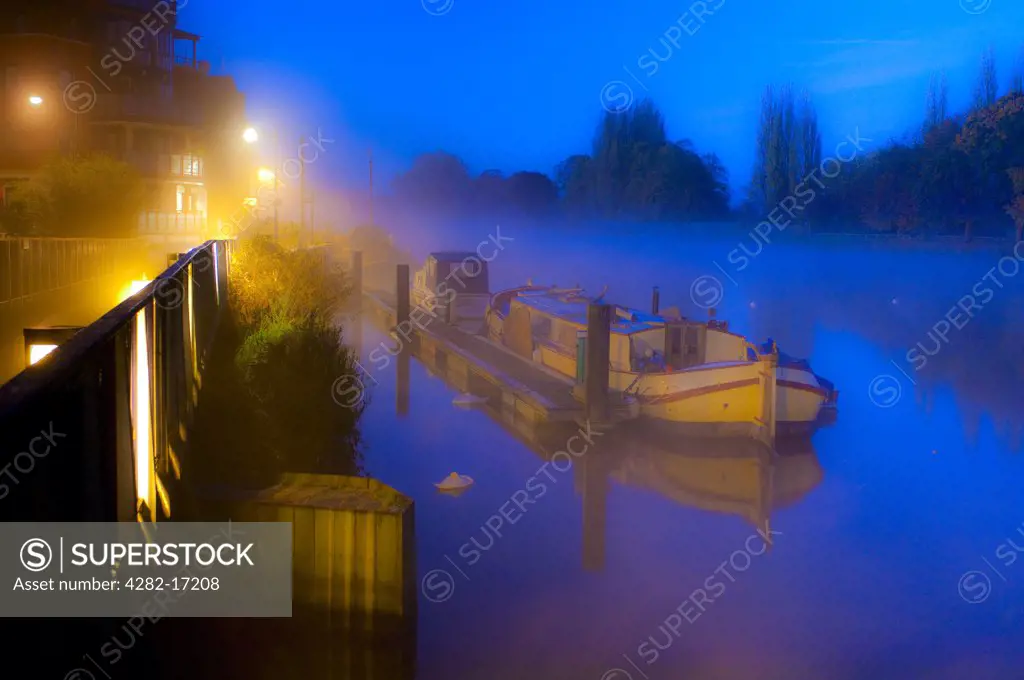 England, Surrey, Kingston Upon Thames. A houseboat moored by a jetty on the River Thames on a foggy morning.