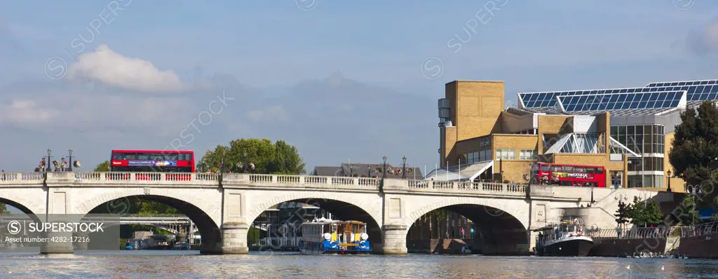 England, Surrey, KIngston upon Thames. Red double decker buses crossing Kingston Bridge over the River Thames as a pleasure boat passes below.