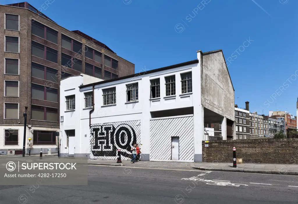 England, London, City of London. Two women walking past a building on Lindsey Street, Smithfield with ""HQ"" painted on shutters by Ben Eine, a street artist notable for his alphabet lettering on shop shutters.