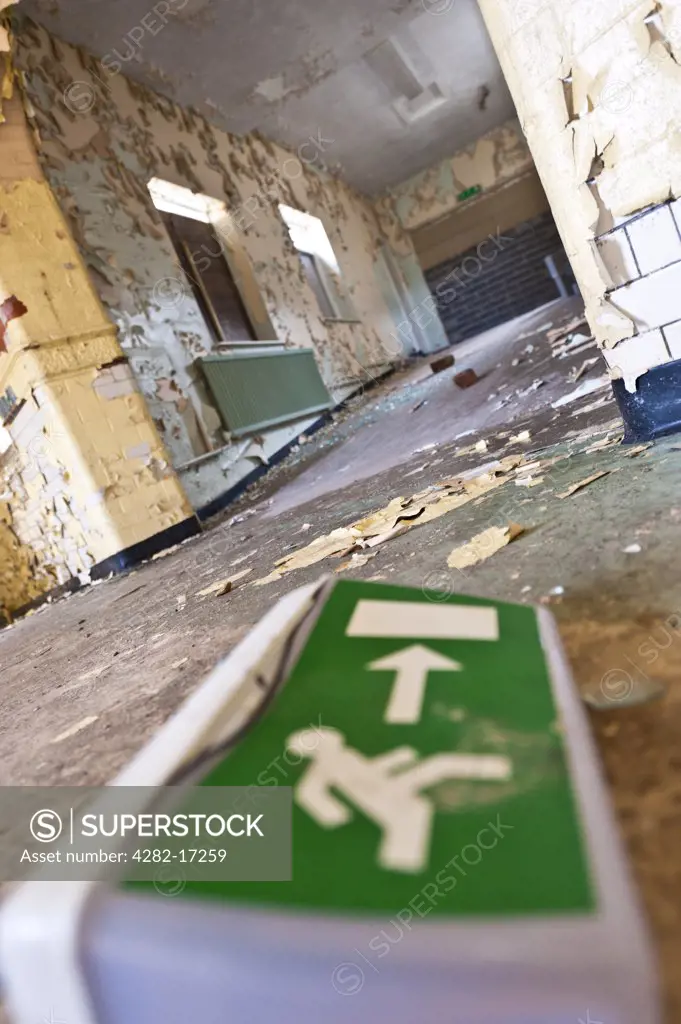 England, West Yorkshire, Leeds. Emergency exit sign on the floor of a derelict hospital, with arrow pointing toward corridor with peeling walls.