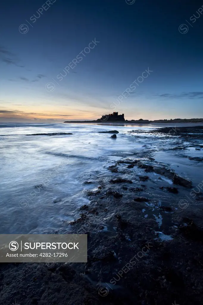 England, Northumberland, Bamburgh. View along the coast at dawn towards Bamburgh Castle, former home to the Kings of Northumbria.