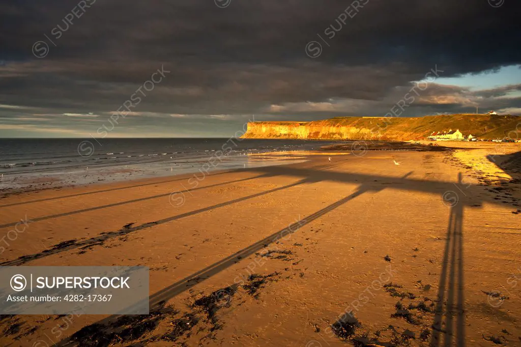 England, Redcar & Cleveland, Saltburn-By-The-Sea. Shadows cast on the beach from the Victorian pier at Saltburn-By-The-Sea, looking towards Huntcliff.