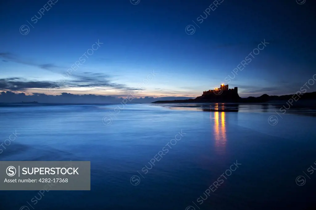 England, Northumberland, Bamburgh. Lights from Bamburgh Castle reflecting in the low tide just before dawn.