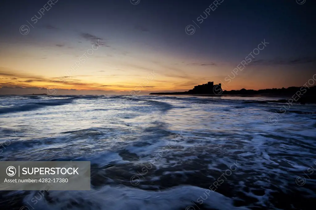 England, Northumberland, Bamburgh. Waves rolling onto the beach by Bamburgh Castle at dawn.