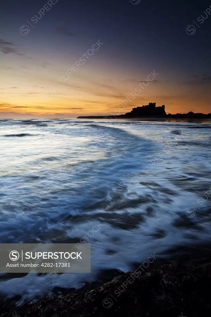 England, Northumberland, Bamburgh. Waves rolling onto the beach by Bamburgh Castle at dawn.