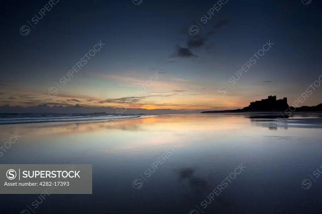 England, Northumberland, Bamburgh. Early dawn light reflected in the glistening shore by Bamburgh Castle.