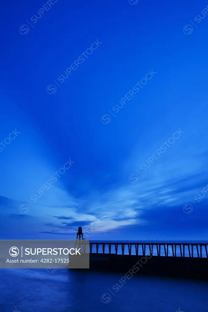 England, North Yorkshire, Whitby. Whitby East Pier Light silhouetted at the end of the East Pier at dawn.
