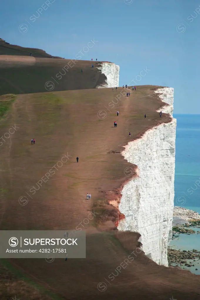 England, East Sussex, Beachy Head. People walking along the cliff top of the massive vertical white chalk sea cliffs near Beachy Head at Birling Gap.