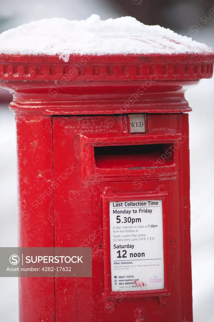 England, London, Merton. Snow on the top of a traditional red post box in South London.