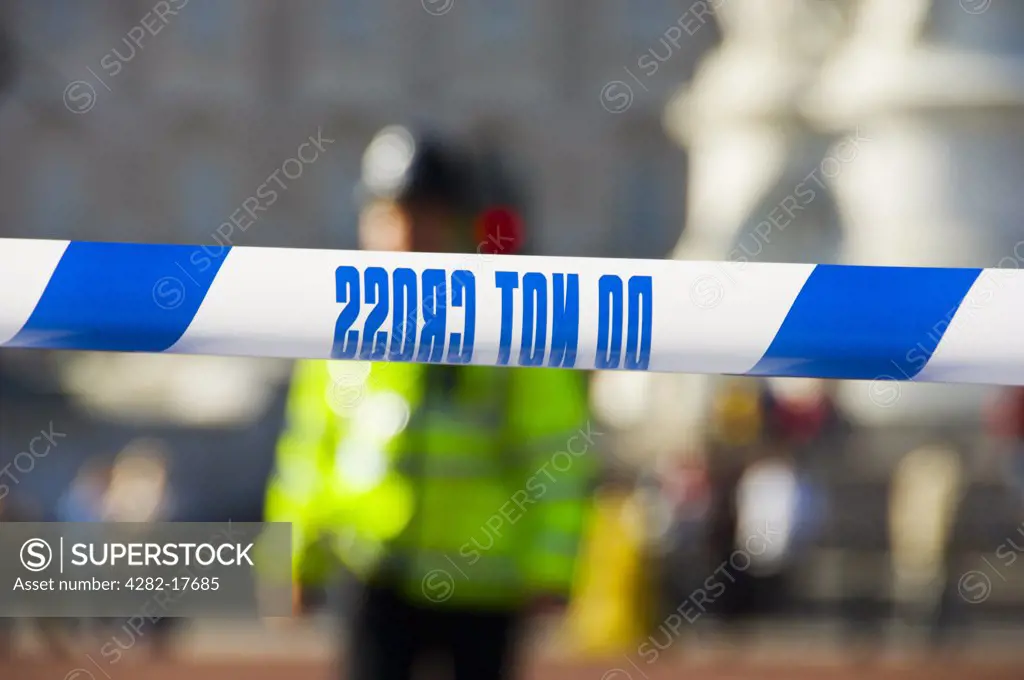 England, London, Westminster. Do Not Cross, Police tape stretched across a road in central London with a metropolitan Policeman wearing a high visibility jacket in the background.