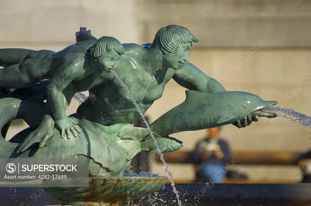 England, London, Trafalgar Square. Water pouring from the mouths of bronze sculptures of mermen and dolphins in a fountain in Trafalgar Square.