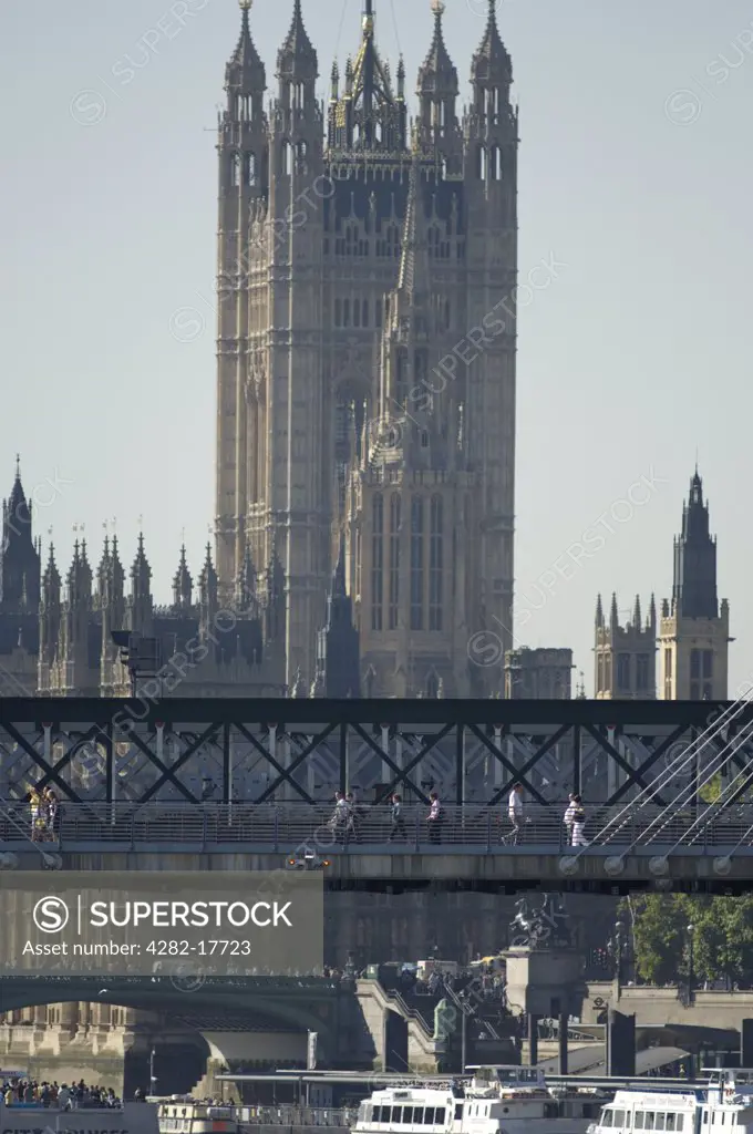 England, London, Westminster. Pedestrians crossing the Golden Jubilee footbridge over the River Thames with the the Houses of Parliament and Westminster Bridge in the background.