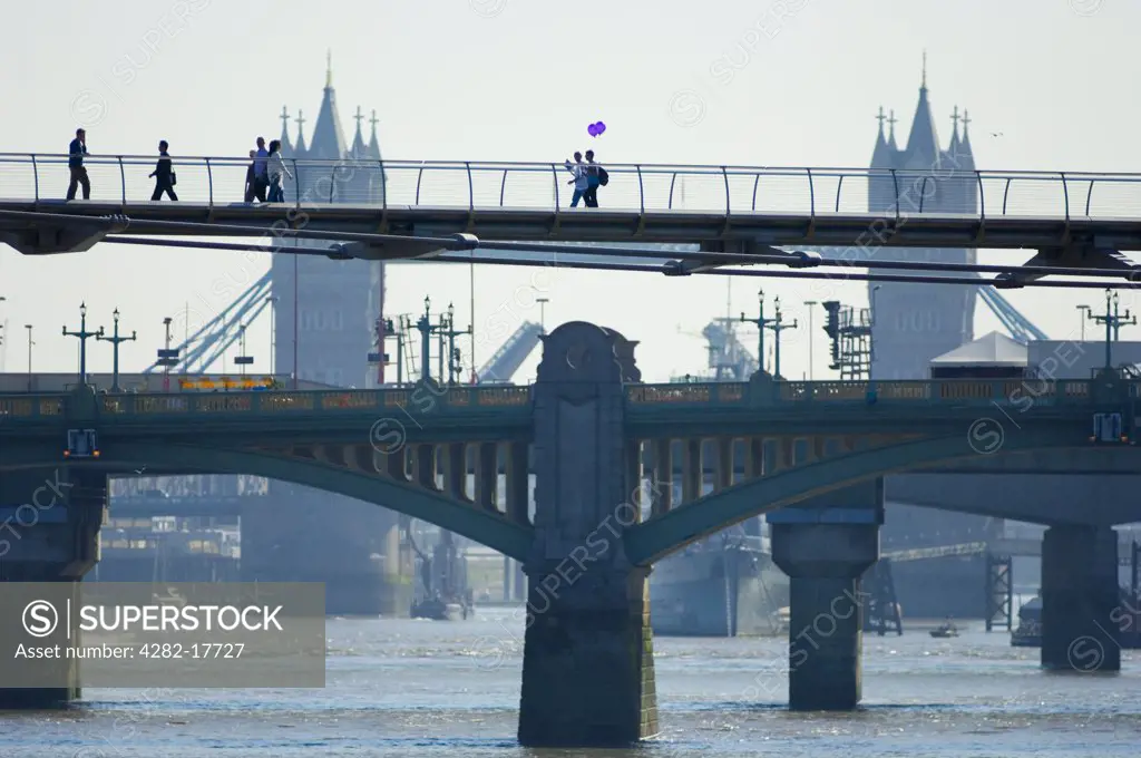 England, London, Millennium Bridge. Pedestrians crossing the Millennium footbridge over the River Thames in central London with Southwark Bridge and Tower Bridge in the background.