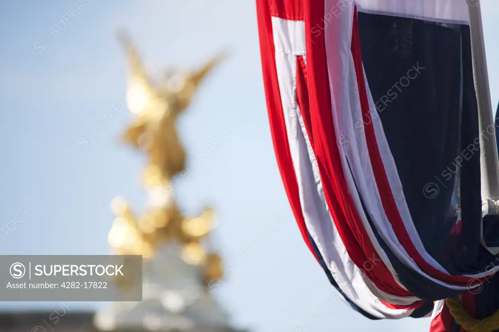 England, London, Westminster. Union Flag hanging from a flag pole on the Royal Wedding route outside Buckingham Palace with the golden statue representing Victory on top of the Victoria Memorial in the background.