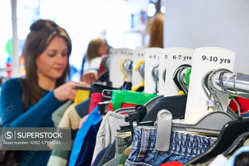 Woman Buying Children's Clothes In Charity Shop