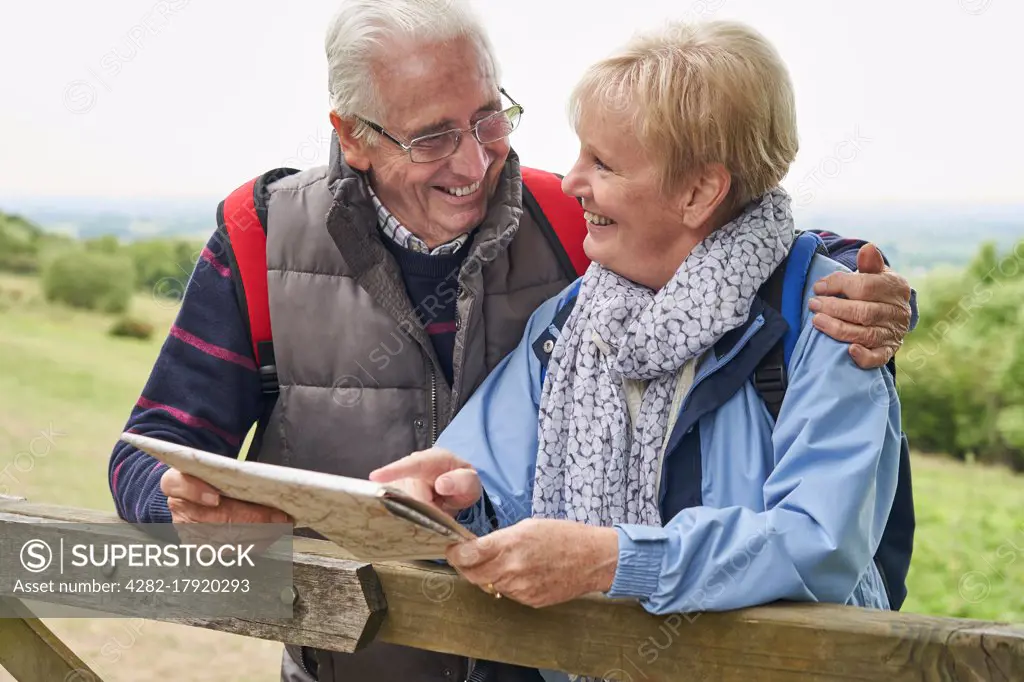 Retired Couple On Walking Holiday Resting On Gate With Map                             
