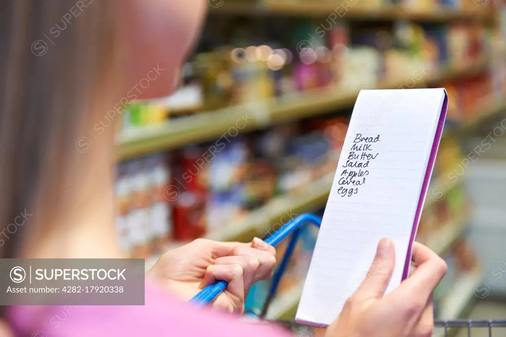 Close Up Of Woman Reading Shopping List In Supermarket