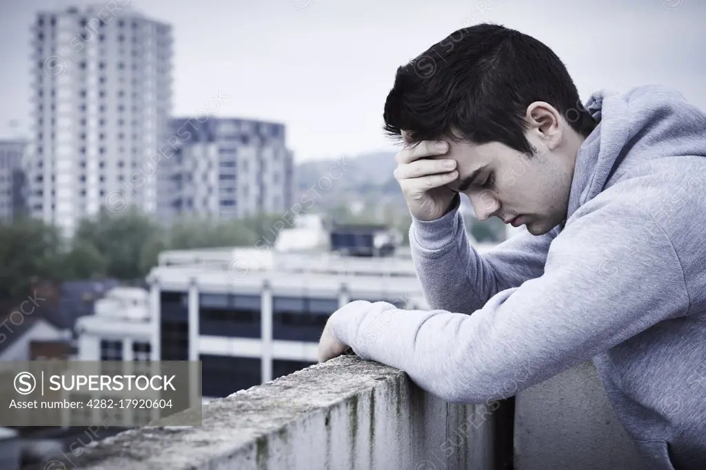 Depressed Young Man Contemplating Suicide On Top Of Tall Building