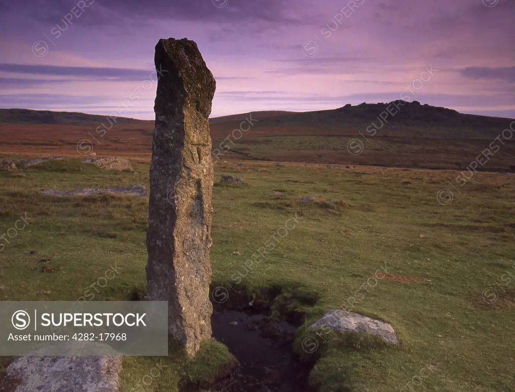 England, Devon, Dartmoor. View of single standing stone in moorland with small tor on the horizon.