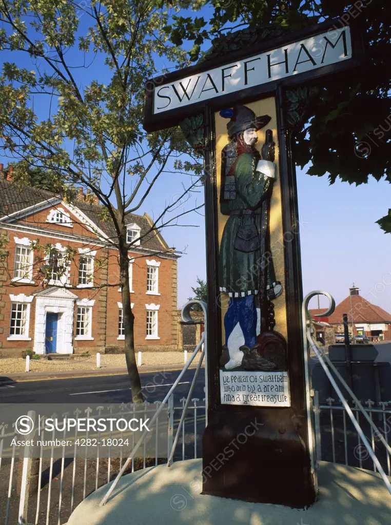 England, Norfolk, Swaffham. Village sign in the Market Place at Swaffham, carved by Harry Carter in 1925. It shows a 14th-century pedlar, John Chapman, who discovered a pot of money buried beneath a tree in his garden as foretold in another man's dream.