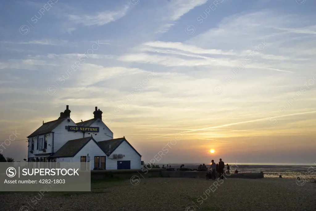 England, Kent, Whitstable. Silhouetted people drinking outside the Neptune pub on the beach at Whitstable in Kent at sunset.