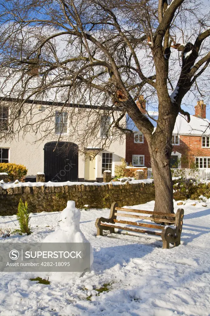 England, Somerset, North Curry. Snowman by a bench in enclosed village green.