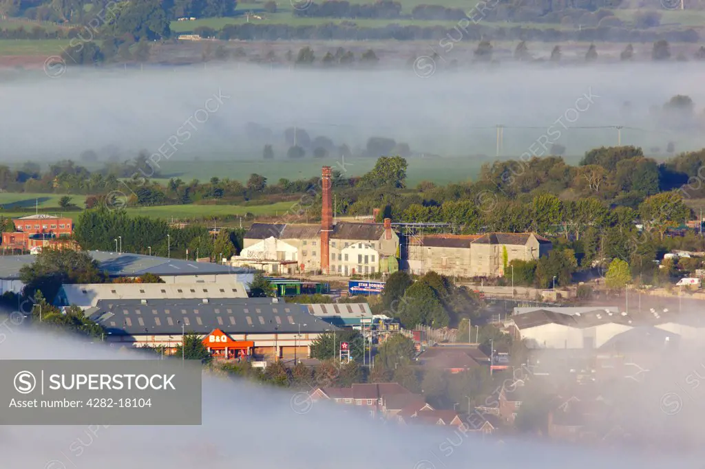 England, Somerset, Glastonbury. View from Glastonbury Tor over mist surrounding retail outlets and old factories near Glastonbury town centre.