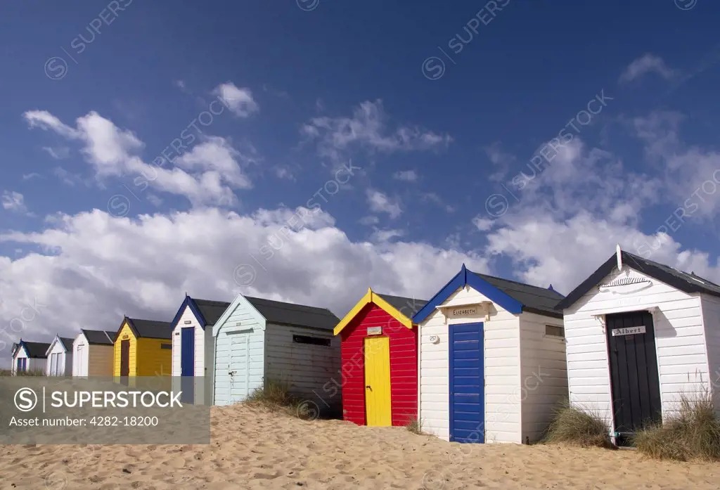 England, Suffolk, Southwold. A line of colourful beach huts on the beach at Southwold.