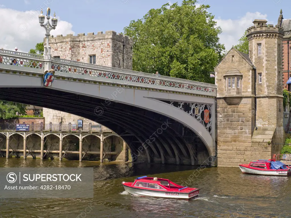 England, North Yorkshire, York. A small pleasure boat passing under Lendal Bridge on the River Ouse by Lendal Tower.
