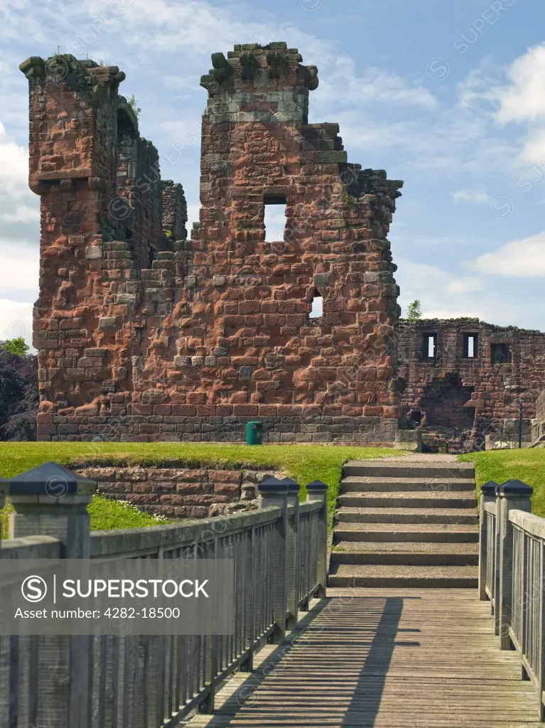 England, Cumbria, Penrith. A wooden footbridge over a moat leading to the ruins of Penrith Castle, once a royal fortress for Richard, Duke of Gloucester before he became King Richard III in 1483.