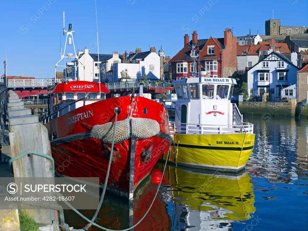 England, North Yorkshire, Whitby. St Mary's Church on East Cliff overlooking fishing boats moored in the harbour.