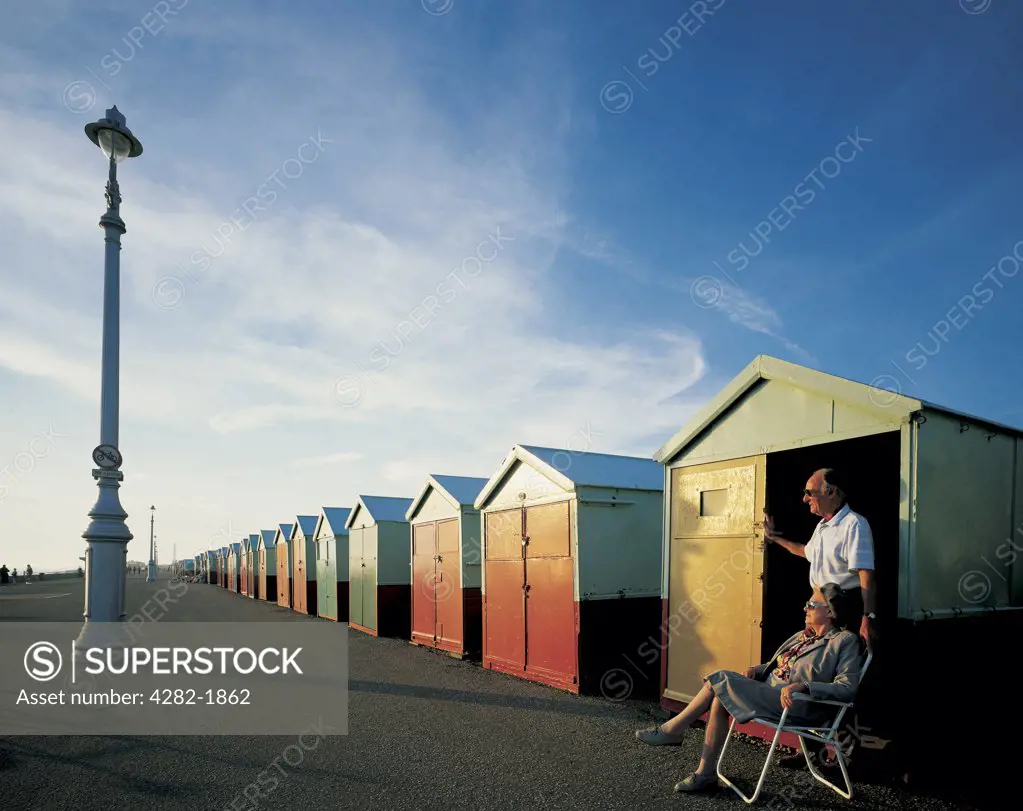 England, East Sussex, Hove. A couple sit outside their beach hut on the promenade at Hove.