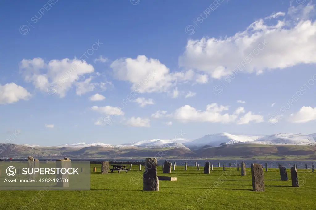 North Wales, Anglesey, Beaumaris. Stone circle on seafront with snow covered mountains in Snowdonia National Park.