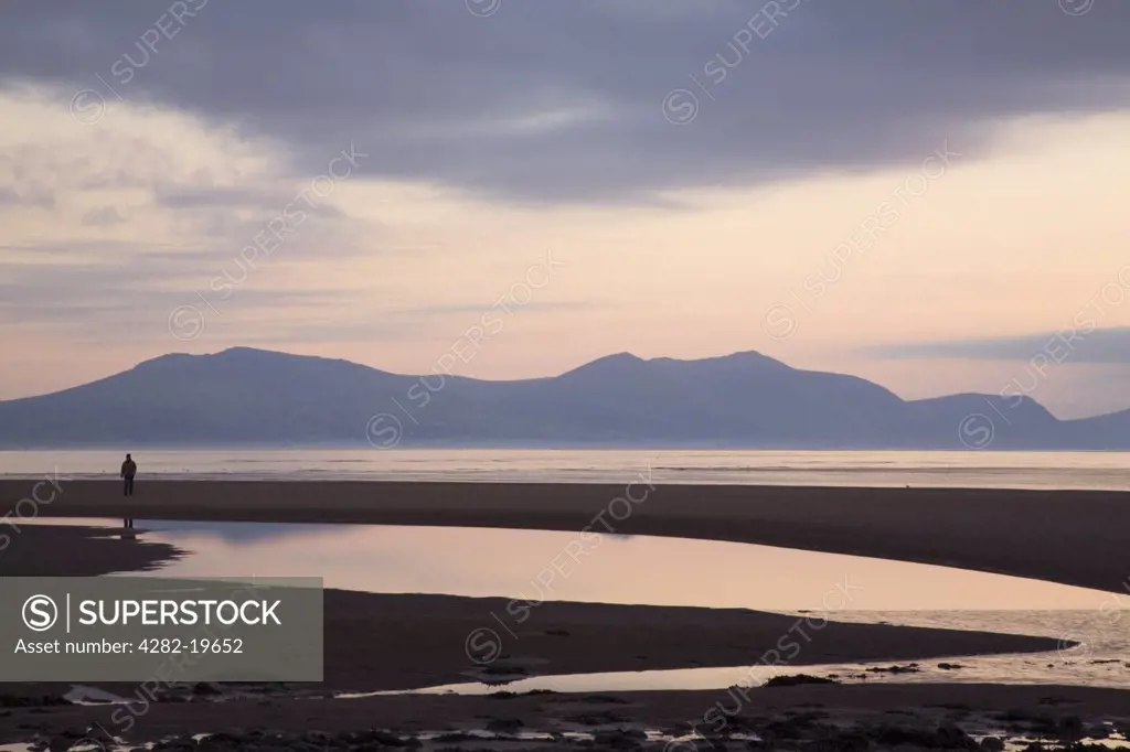 North Wales, Anglesey, Newborough. A view toward the Lleyn Peninsula with a lone man on the beach.