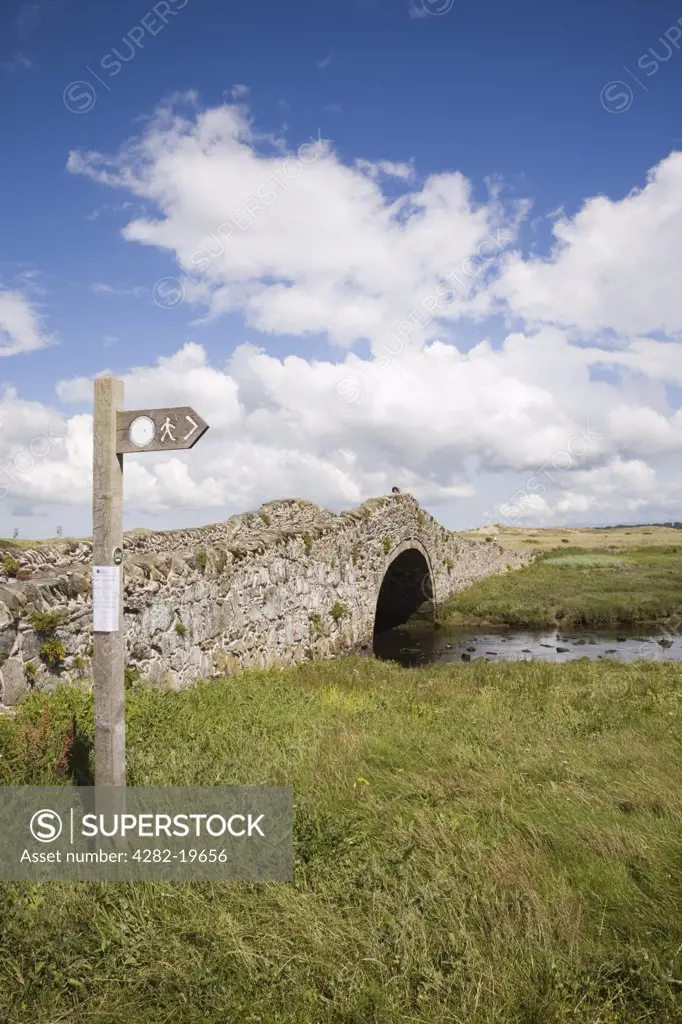North Wales, Anglesey, Aberffraw. An old stone bridge across the Afon Ffraw river with Isle of Anglesey Coastal Footpath sign.