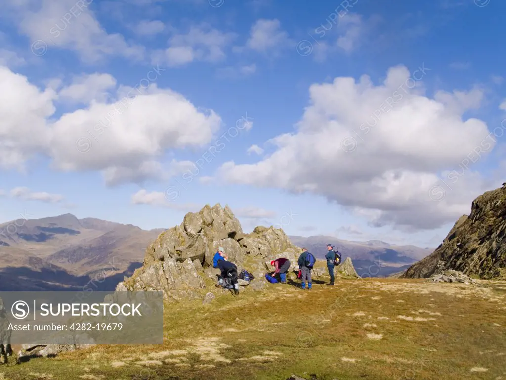 North Wales, Snowdonia, Cnicht. A group of walkers resting by rocks on the path up to Cnicht mountain with a view to Snowdon horseshoe beyond in Snowdonia National Park.