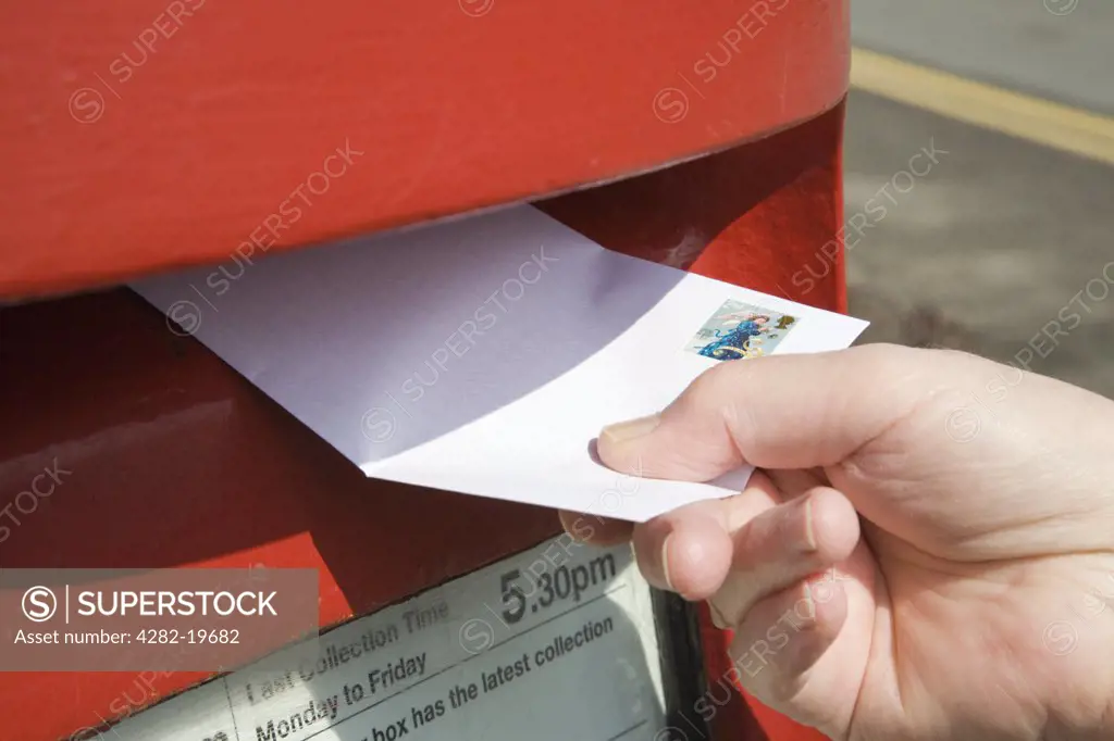 North Wales, Anglesey, Llangefni. A close-up of a person posting a letter in a traditional red postbox.