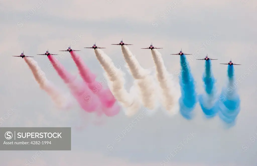 England, Kent, Biggin Hill. Royal Air Force Red Arrows aerobatic display team made up of British Aerospace Hawk T1 jet training aircraft performing a colourful fly past at Biggin Hill.