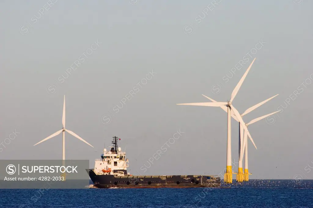 England, Norfolk, Great Yarmouth. A cargo ship, the Olympic Provider passing in front of an offshore wind farm at Great Yarmouth in Norfolk.