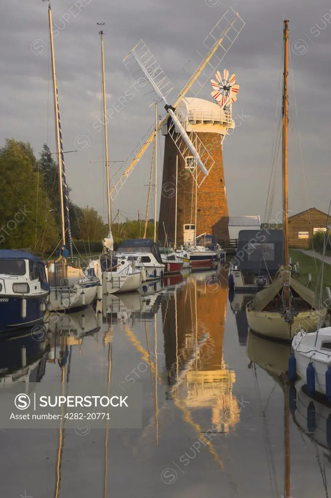 England, Norfolk, Horsey. Last rays of late afternoon sunlight over boats on the Norfolk Broads by Horsey Windpump, a fully restored historic drainage windpump.