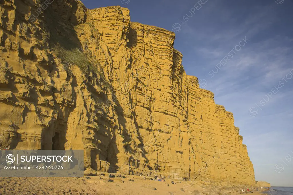 England, Dorset, West Bay. People on the beach below the sandstone East Cliff of West Bay on the Jurassic Coast in Dorset.