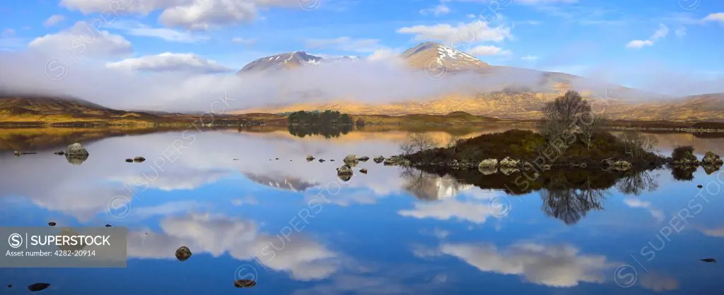Scotland, Argyll and Bute, Rannoch Moor. A panoramic view of Lochan na h-Achlaise featuring a rare combination of clouds, mirror reflections, and mist slowly clearing the surrounding mountains on Rannoch Moor.