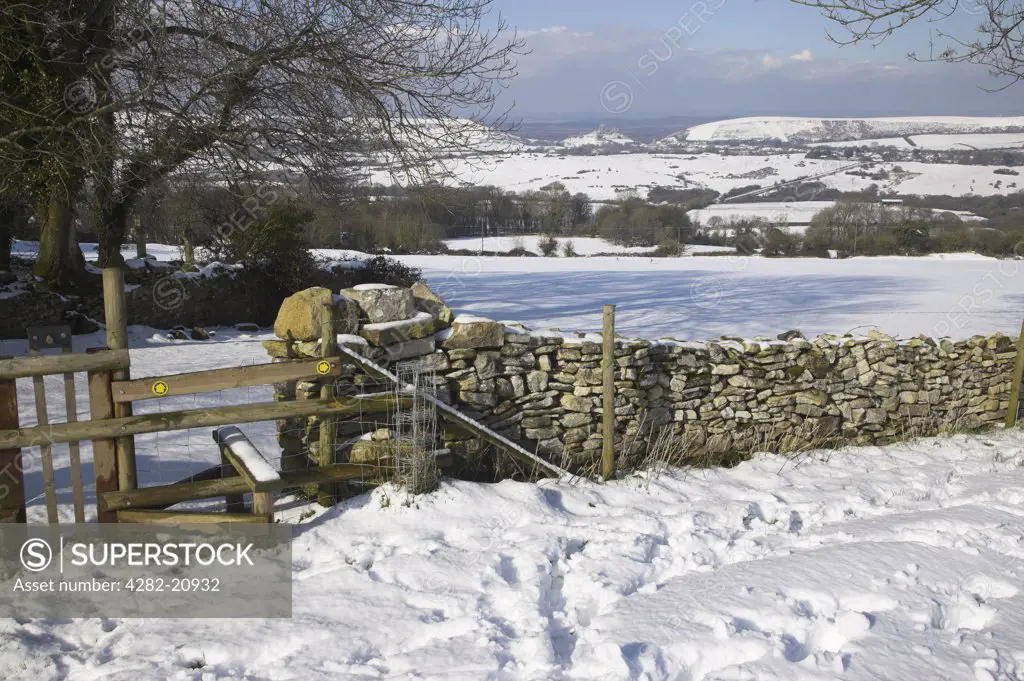 England, Dorset, Corfe Castle. View from a stile in a stone wall in the village of Kingstone looking towards Corfe Castle across the Purbeck Hills after a heavy snow fall in March.