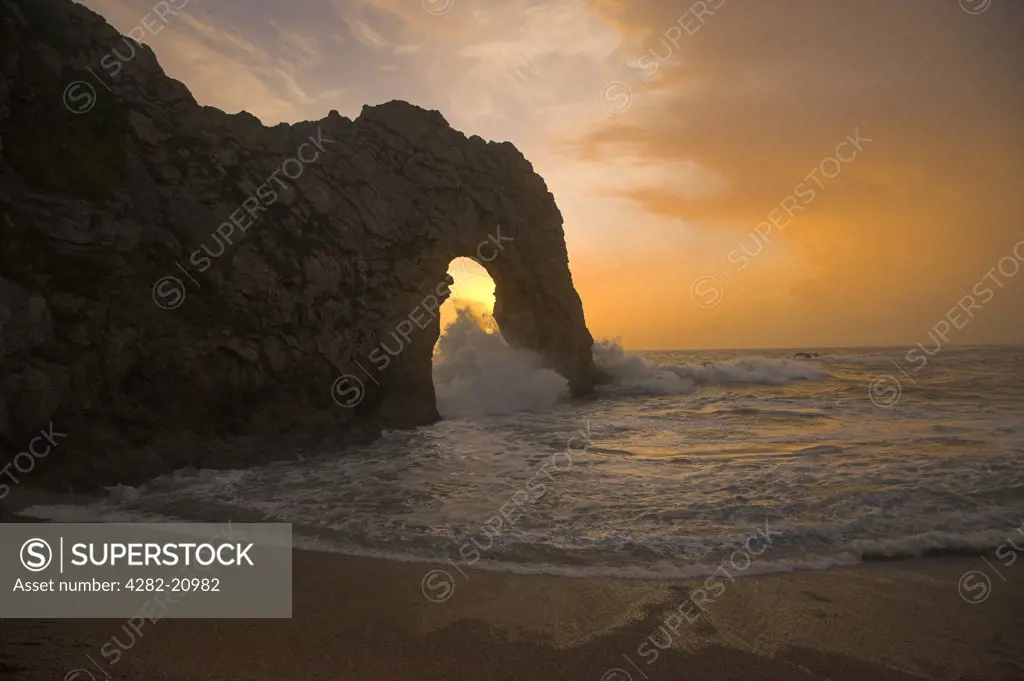 England, Dorset, Durdle Door. Sun setting through the natural limestone arch at Durdle Door on the Jurassic coast in Dorset.
